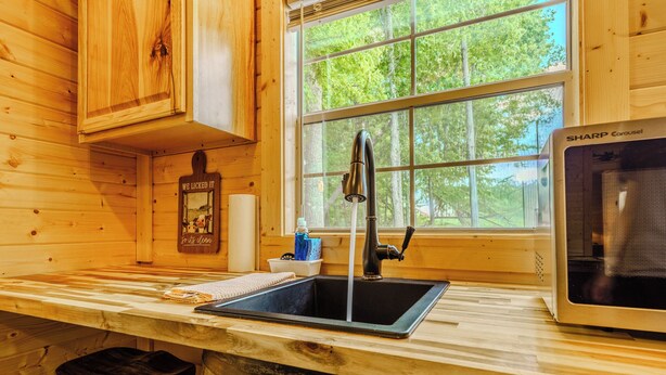 L’intérieur d’une cabane en bois comprend un coin cuisine équipé d’un évier, d’un robinet et d’un four à micro-ondes.