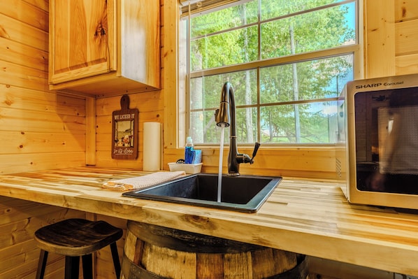 A wooden cabin interior with a kitchen area featuring a sink, faucet, and a microwave. - 10 Minutes from downtown Sevierville. Firefly Cottage (Sevierville)