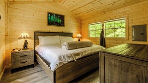 Een slaapkamer in een houten hutje, met een bed, nachtkastjes, een schilderij en een raam.