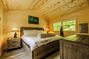 A wooden cabin bedroom with a bed, nightstands, a painting, and a window. - 10 Minutes from downtown Sevierville. Firefly Cottage (Sevierville)
