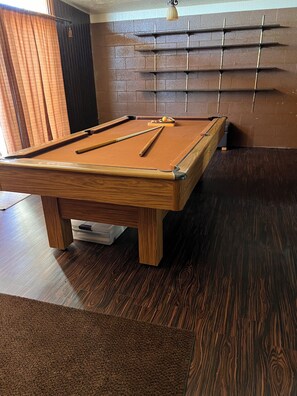 A pool table with a wooden frame, a dark wooden floor, and a brick-patterned wall. - Large home located in the countryside with swimming pool and backyard pool room. (Woodland)