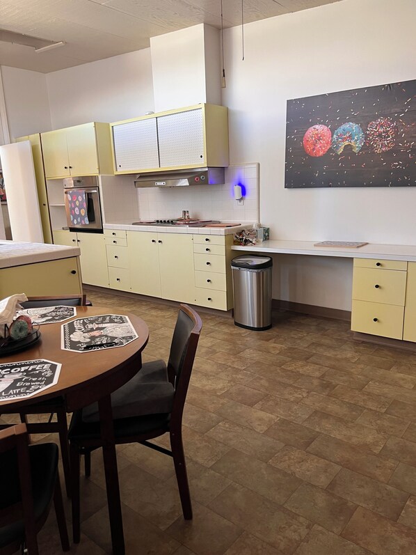 A modern kitchen with a dining area, featuring a stainless steel refrigerator, a microwave, and a sink. There is a trash can and a wall-mounted light fixture. - Large home located in the countryside with swimming pool and backyard pool room. (Woodland)