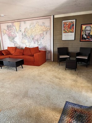 A room with a large world map, a red sofa, two wicker chairs, and a framed artwork on the wall. - Large home located in the countryside with swimming pool and backyard pool room. (Woodland)