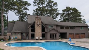 Une maison à deux étages avec une piscine, une cheminée en briques et un garage avec des portes en bois.