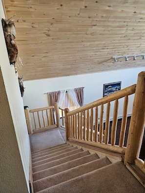 Eine Holztreppe mit Handlauf, Teppichstufen und einer Decke mit Holzbalken.