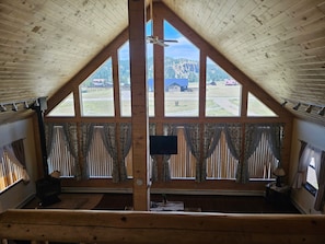 Ein Zimmer mit hohen Decken, großen Fenstern, einem Deckenventilator und Blick auf eine ländliche Landschaft.