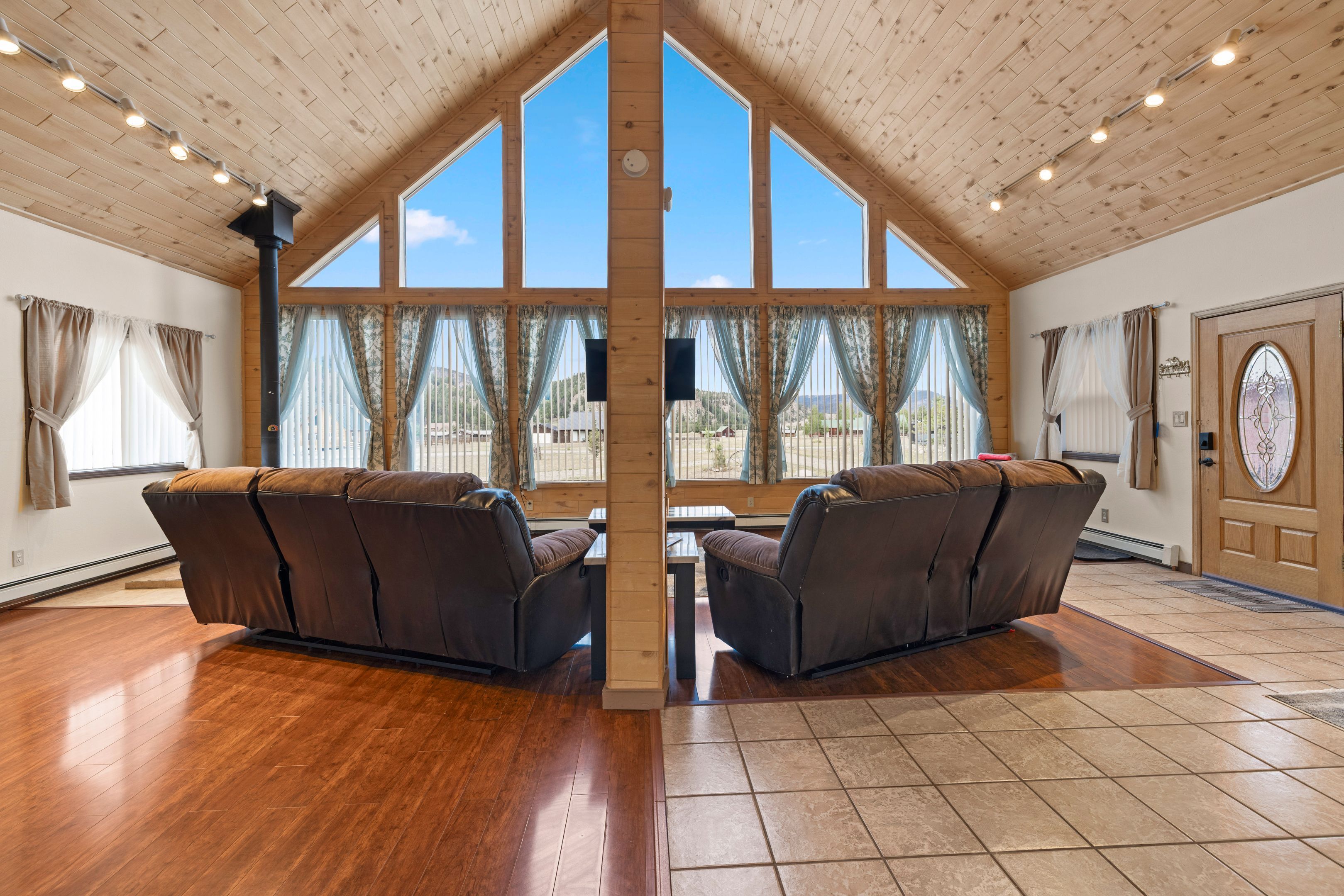 A room with a sloped ceiling, large windows, two leather sofas, and a wooden door.