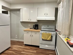Una cocina compacta con armarios blancos, estufa y cafetera.