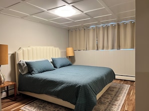 Un dormitorio con cama, mesita de noche, lámpara, ventana con cortinas y radiador.