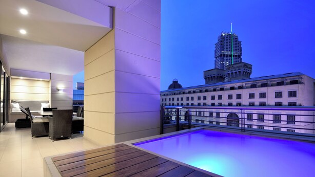 A modern rooftop terrace with a pool, seating area, and a view of a cityscape including a distinctive building. - The Raphael Penthouse Suites (Johannesburg)