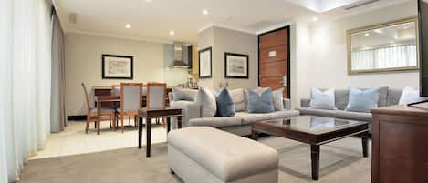 A modern living room with a sofa, ottoman, coffee table, and dining area.