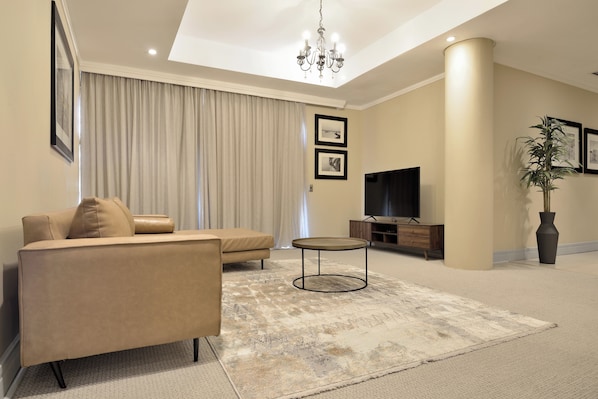 A modern living room with a sofa, a coffee table, a flat-screen TV, and a large plant. - The Raphael Penthouse Suites (Johannesburg)