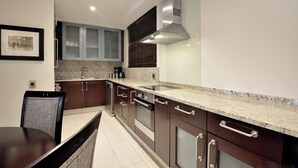 A modern kitchen with dark wooden cabinets, a granite countertop, stainless steel appliances, and a framed picture on the wall. - The Raphael Penthouse Suites (Johannesburg)