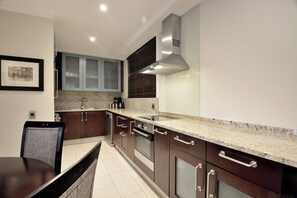 A modern kitchen with dark wooden cabinets, a granite countertop, stainless steel appliances, and a framed picture on the wall. - The Raphael Penthouse Suites (Johannesburg)
