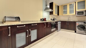 A modern kitchen with dark wooden cabinets, a stainless steel range hood, a built-in microwave, and a dishwasher. - The Raphael Penthouse Suites (Johannesburg)