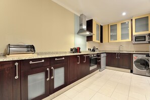 A modern kitchen with dark wooden cabinets, a stainless steel range hood, a built-in microwave, and a dishwasher. - The Raphael Penthouse Suites (Johannesburg)