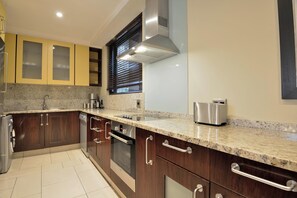 A modern kitchen with granite countertops, stainless steel appliances, and wooden cabinets. - The Raphael Penthouse Suites (Johannesburg)