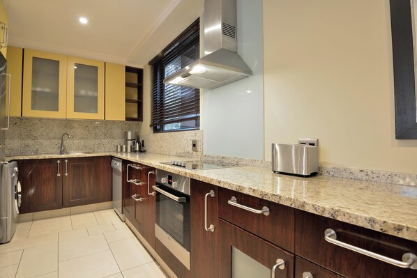 A modern kitchen with granite countertops, stainless steel appliances, and wooden cabinets. - The Raphael Penthouse Suites (Johannesburg)