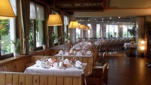 A restaurant with multiple tables set for dining, large windows, and indoor plants. - Hotel Landhof Simeter Gmbh (Spittal an der Drau)