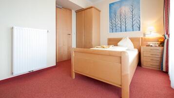 Een slaapkamer met een bed, een kledingkast, een radiator, een schilderij en een nachtkastje met een lamp.
