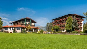A hotel with a traditional Alpine architectural style, featuring multiple balconies with flower boxes, set against a backdrop of lush green fields and mountains. - Hotel Landhof Simeter Gmbh (Spittal an der Drau)