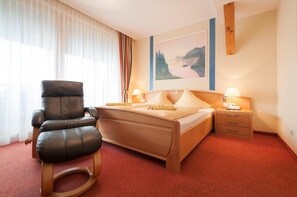 A hotel room with a bed, a leather chair, a nightstand, and a painting on the wall. - Hotel Landhof Simeter Gmbh (Spittal an der Drau)