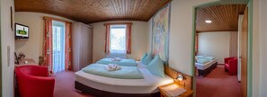 A bedroom with two beds, a red chair, and a wooden ceiling. - Hotel Landhof Simeter Gmbh (Spittal an der Drau)