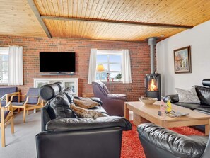 Una sala de estar acogedora con pared de ladrillo, chimenea, televisor y mobiliario de cuero.