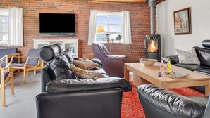 Ein gemütliches Wohnzimmer mit Kamin, Ledersofas, Fernseher und einer Ziegelwand.