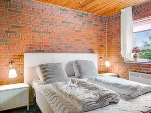 A bedroom with a brick wall, a white headboard, two bedside lamps, a window with a curtain, and a radiator. - 4 Star Holiday Home in Hjorring (Hjørring)