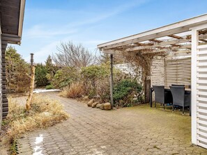 En täckt uteplats med en pergola, utomhusmöbler och en gångstig av sten.