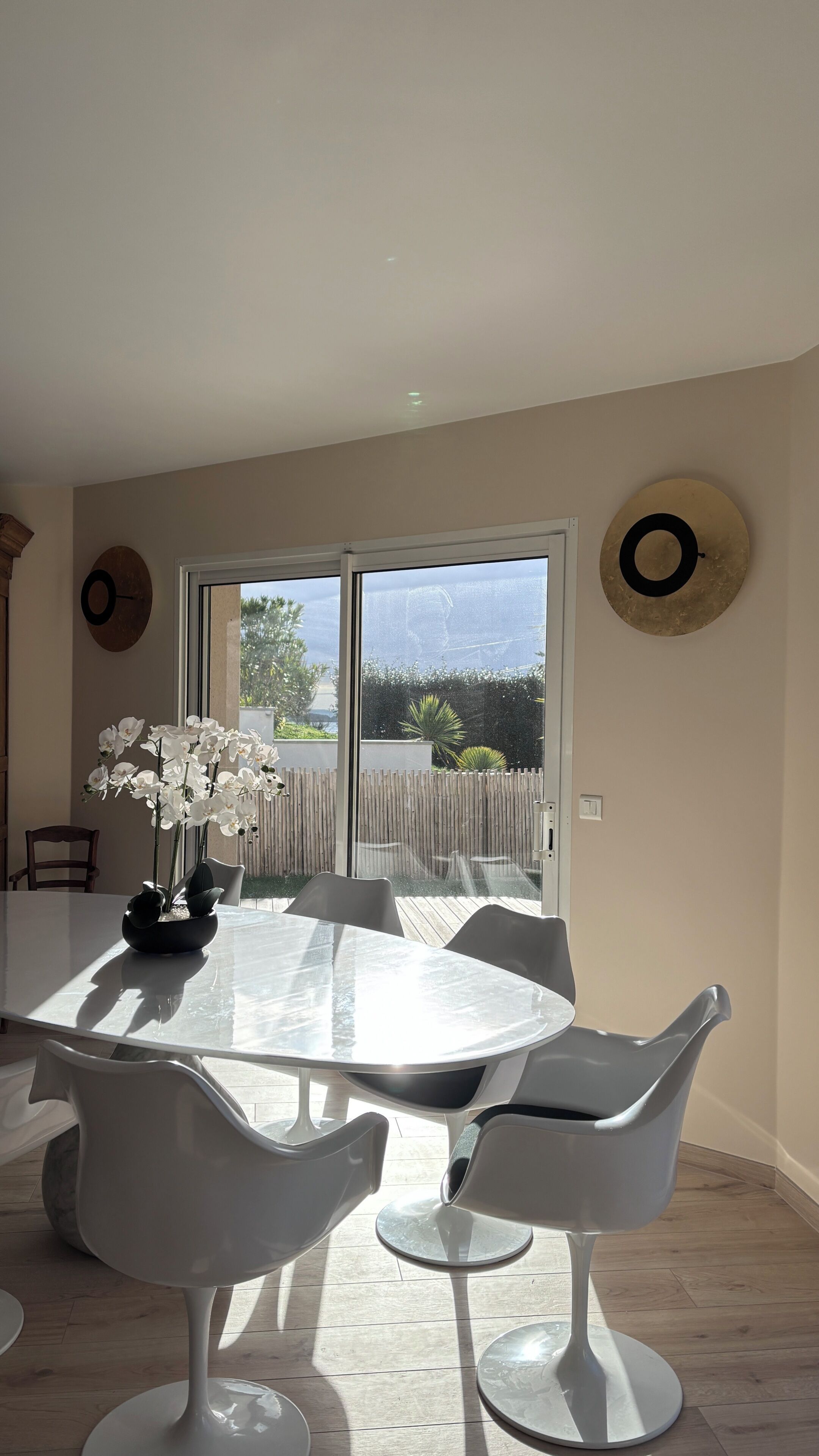 A dining area with a round table, white chairs, and a potted plant.