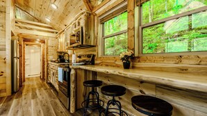 Interior de una cabaña de madera con cocina, zona de bar y ventanas amplias.