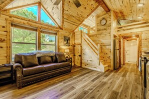 A log cabin interior with a leather sofa, wooden floors, a staircase, and a kitchen area. -  7 minutes from Soaky Mtn Waterpark. Mountain Escape Cabin (Sevierville)
