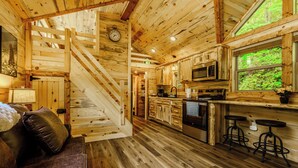 Interior de una cabaña de madera con cocina, comedor y una escalera.