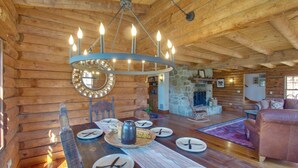 A log cabin interior with a dining table set for four, a stone fireplace, and a wooden ceiling.