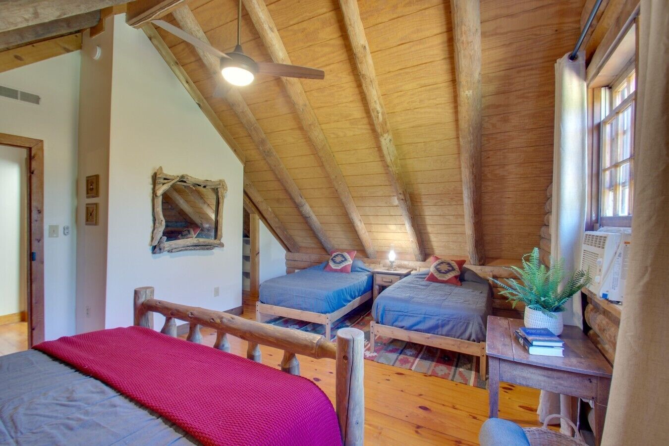 A cozy attic bedroom with two beds, a ceiling fan, and a window with curtains.