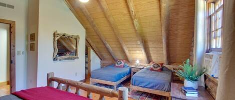 A cozy attic bedroom with two beds, a ceiling fan, and a window with curtains.