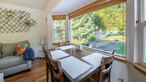 Un espace repas comprenant une table, des chaises et une vue sur un jardin, grâce à de grandes fenêtres.