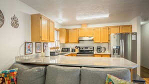 Une cuisine moderne avec des meubles en bois, un réfrigérateur en acier inoxydable et un grand îlot central doté d’un plan de travail en marbre.