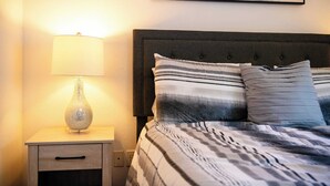 Un lit bien fait, avec une literie à rayures, une lampe de chevet et une œuvre d’art accrochée au mur.