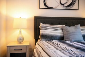 Uma cama bem arrumada com roupa de cama listrada, uma luminária de cabeceira e uma obra de arte na parede.