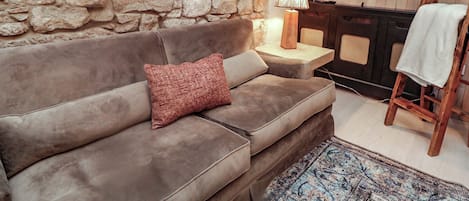 Un salon avec un mur en pierre, un canapé marron, une lampe, un téléviseur et une petite table.