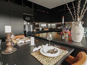 A modern kitchen with a central island, a dining area with a table set for two, and a view of the kitchen in the background. - HANOWEN  HOUSE, pet friendly, with hot tub in Dungloe, County Donegal (Dungloe)