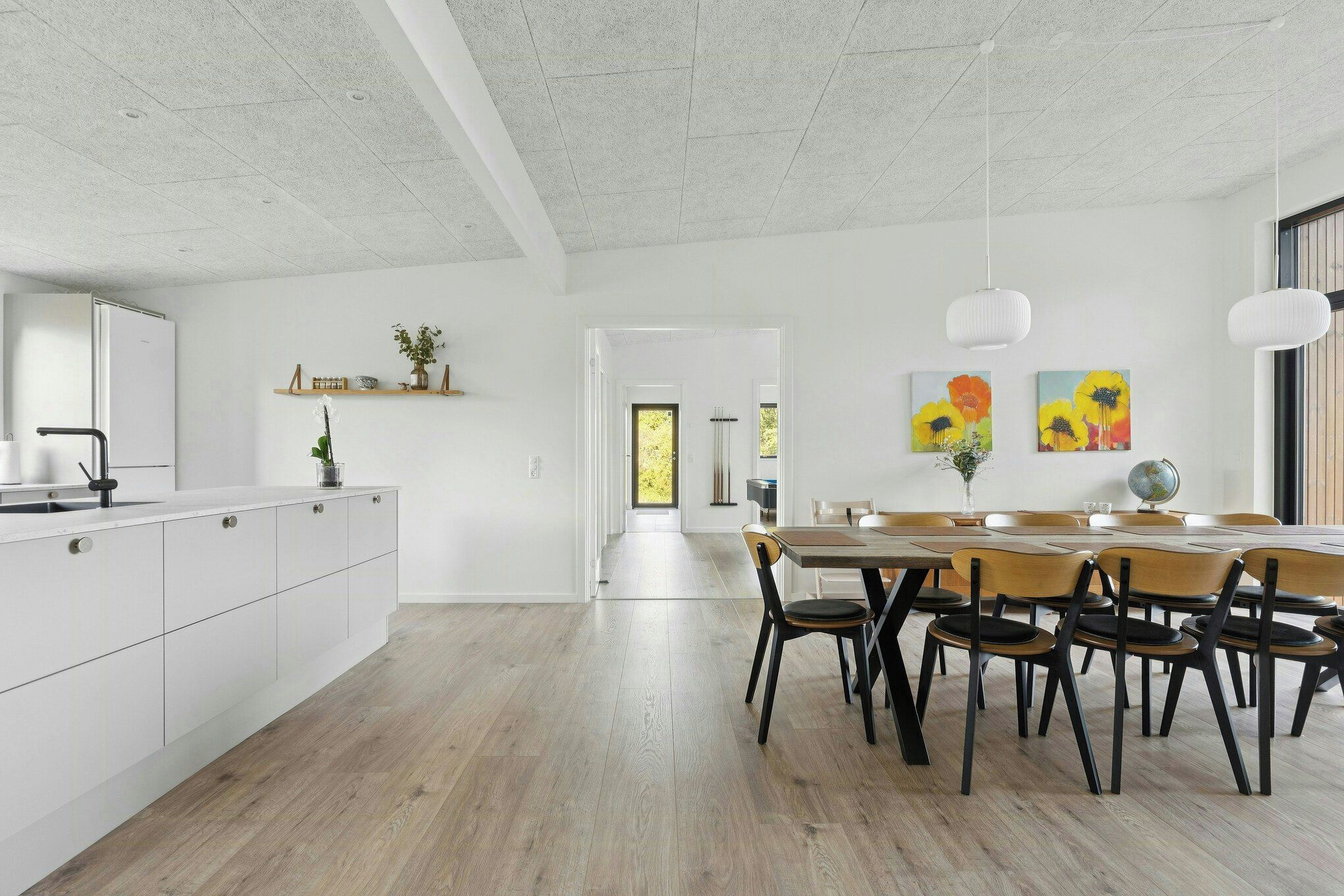 Una cocina moderna con muebles blancos, una mesa de comedor de madera y sillas. Se puede ver el área de comedor a través de una puerta abierta.