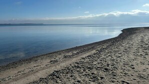 A beach with a pebbly shoreline and calm water extending to the horizon. - House on large nature plot with sea view and spa (Broager)