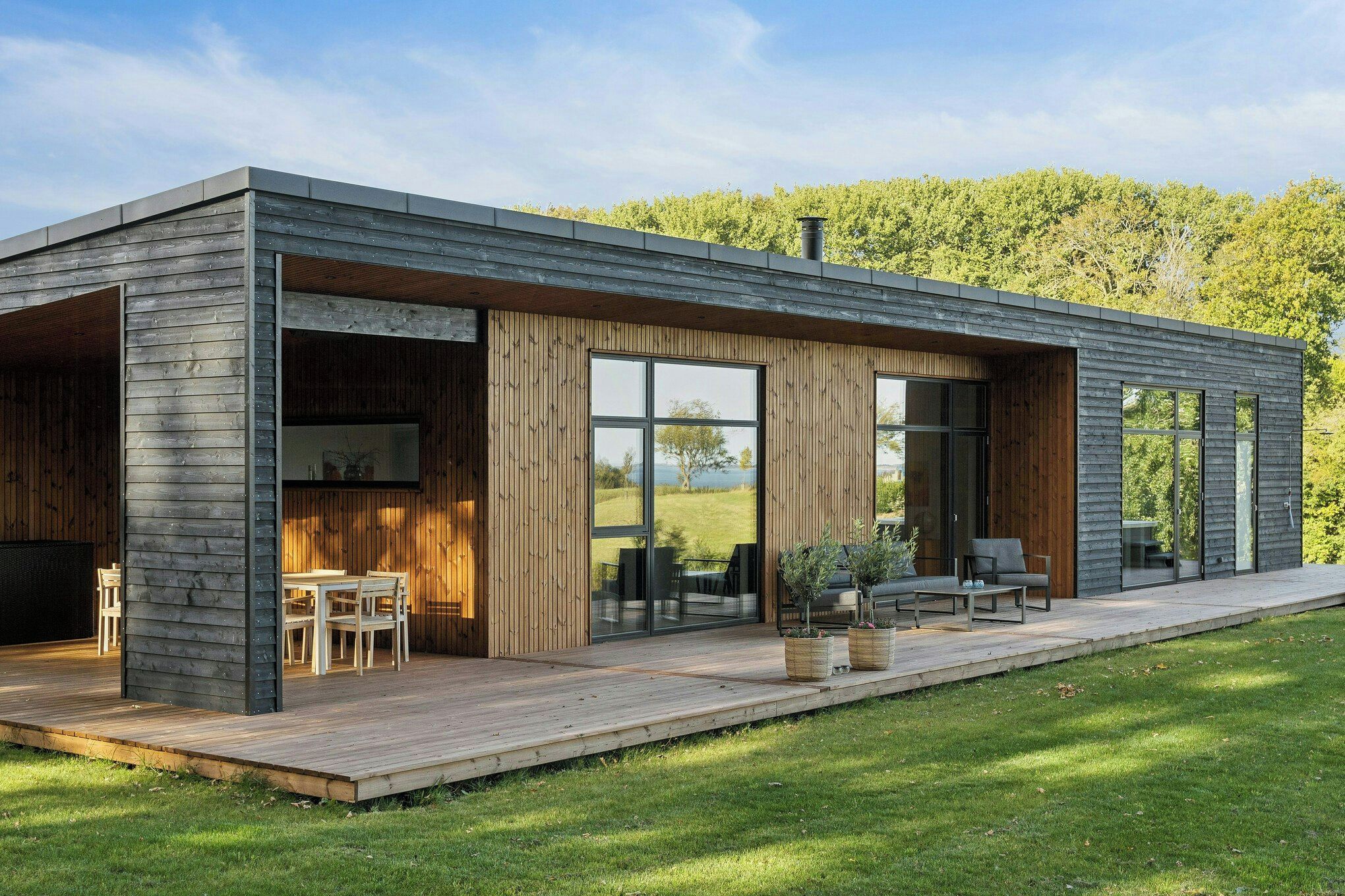 A modern house with a deck, large windows, and a view of the surrounding greenery.