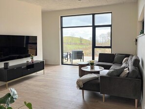 En moderne stue med stort TV, sofa, sofabord og udsigt gennem et stort vindue.