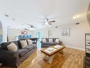 Ein Wohnzimmer mit zwei Sofas, einem Couchtisch, Deckenventilatoren und einem Essbereich mit Stühlen und einem Tisch.