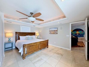 Ein Schlafzimmer mit einem hölzernen Bett, einem Deckenventilator, einem Nachttisch mit Lampe und einem Bild an der Wand.